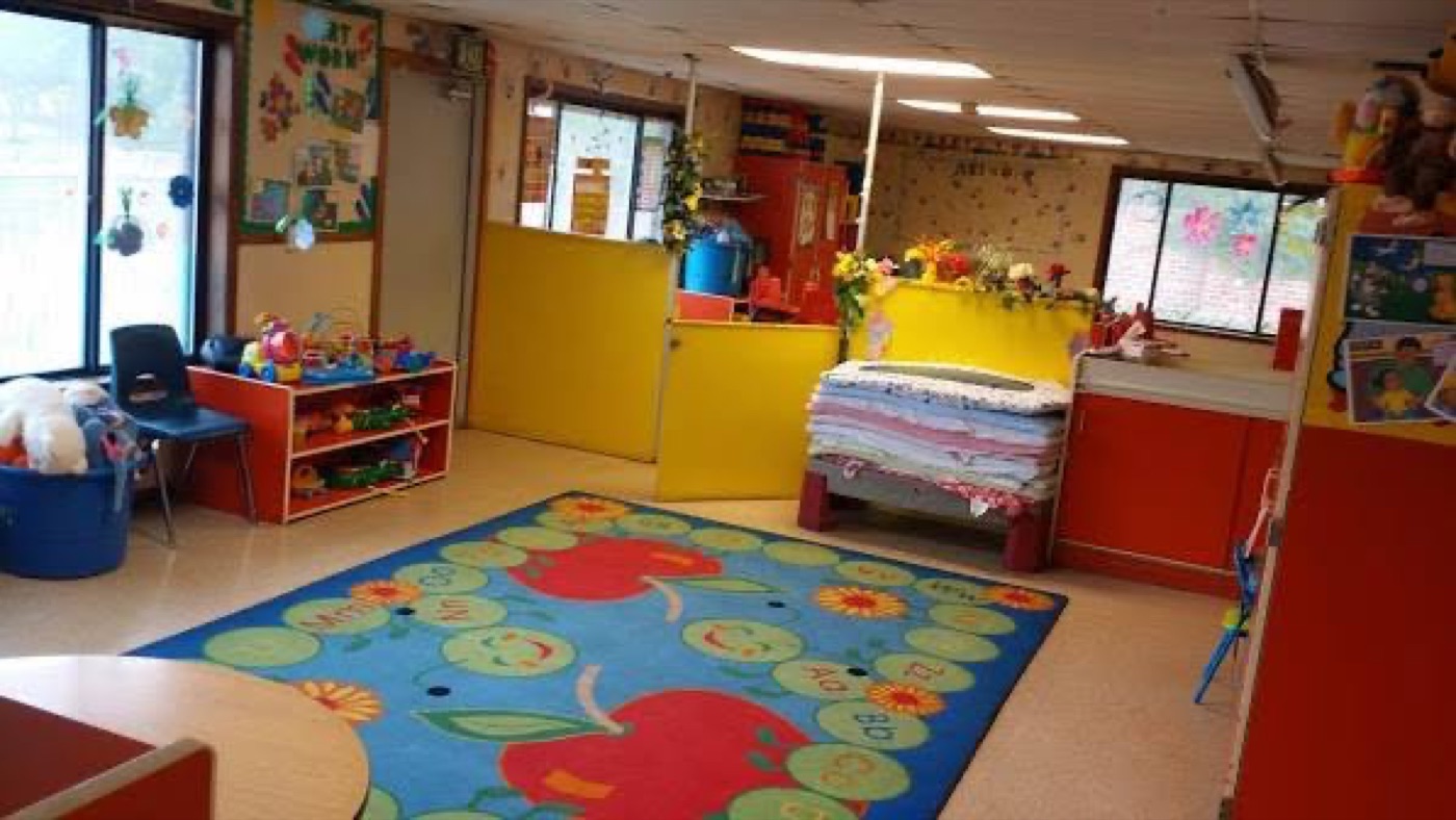 Learning area with alphabet caterpillar rug, toy shelves, and cozy classroom spaces